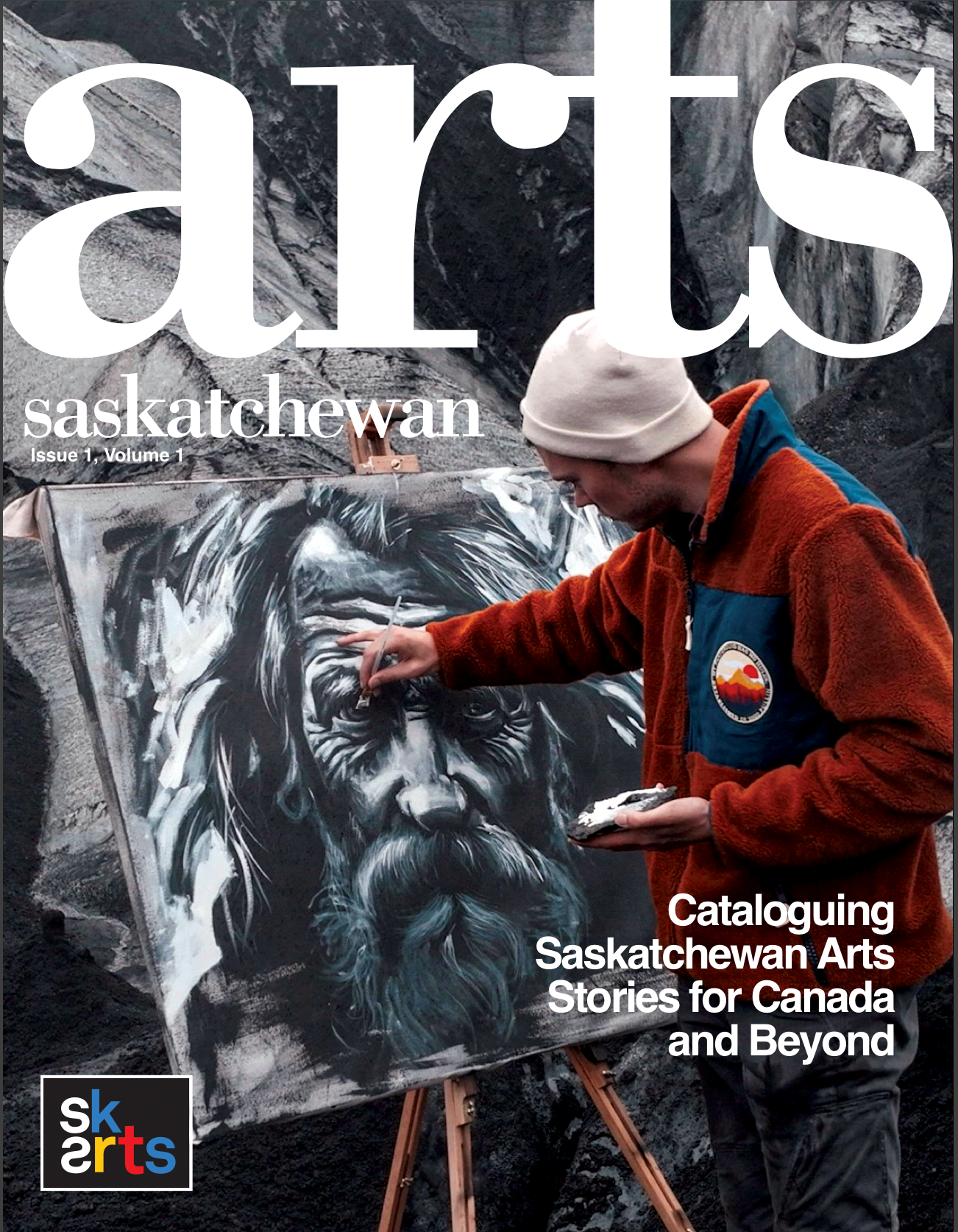 SK Arts' arts magazine Arts Saskatchewan 2024 cover. [IMAGE]: Young male visual artist Andrew Robertson on a glacier in Iceland painting the artwork, stöðugt, 2024 ( a profile of a hardened farmer with long hair and a beard). Photo credit: Adler Irwin of Irwin Films. [TEXT]: Arts Saskatchewan, Issue 1, Volume 1. Cataloguing Saskatchewan Arts Stories for Canada and Beyond. [IMAGE]: SK Arts logo. 