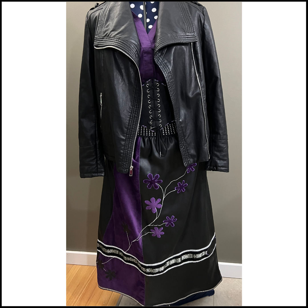  Black and purple story skirt, designed by Nancy Lafleur on a hanger with a leather jacket in front of a gray wall.