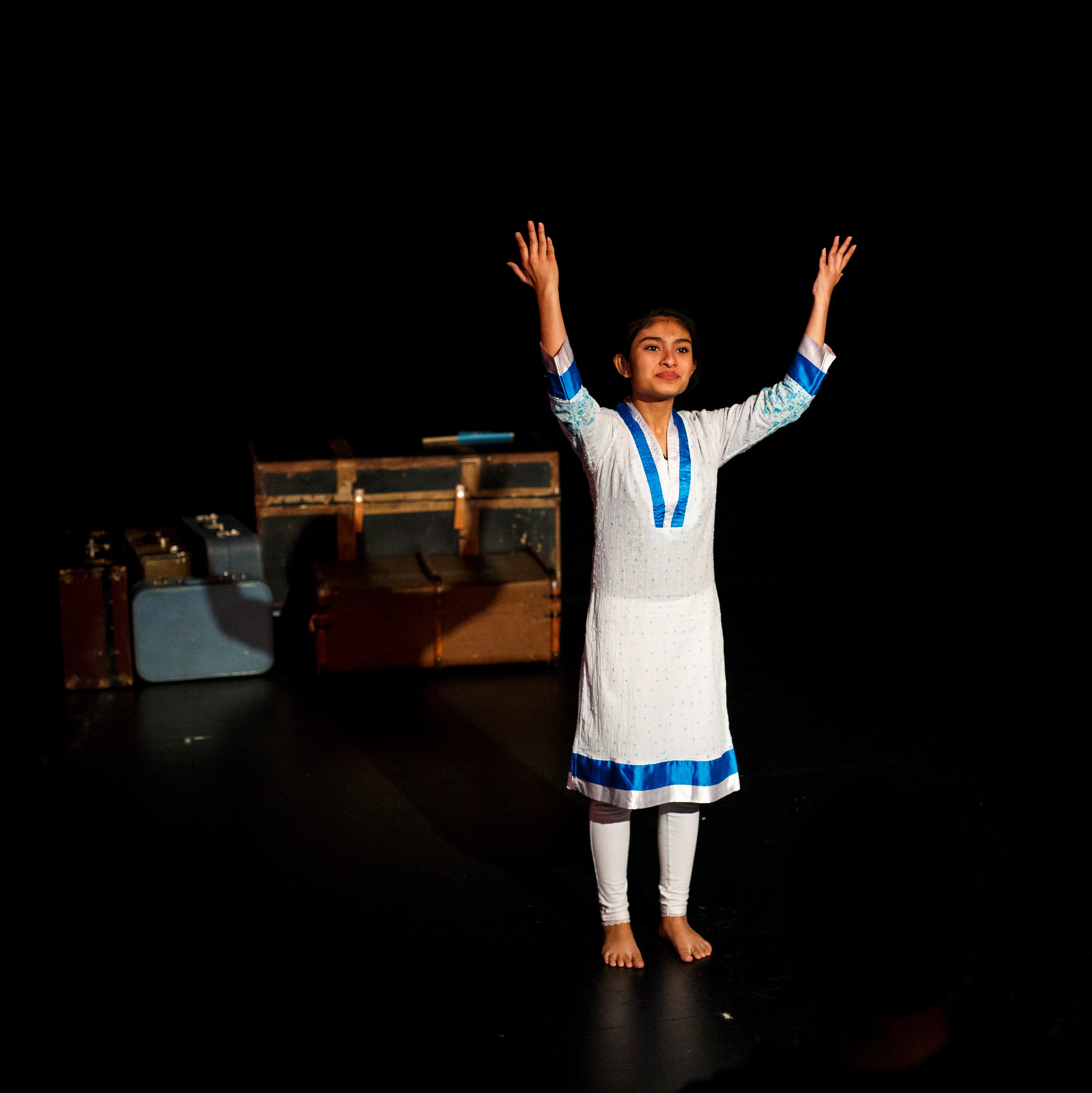 Fatima Nafisa - Young woman on stage in traditional Indian wear. White pants and long shirt with blue trim.