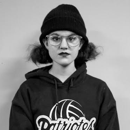Kam Miller by Cory Dallas StandingKam Miller, 75th anniversary nominee. Young girl in black and white photo wearing a beanie, glasses, a hoodie and lipstick. Her hair is in buns.