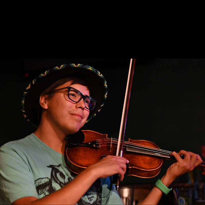 Tristen Durocher , SK Arts 75th anniversary nominee - Man wearing sombrero and playing the fiddle. He is wearing glasses and a green shirt.