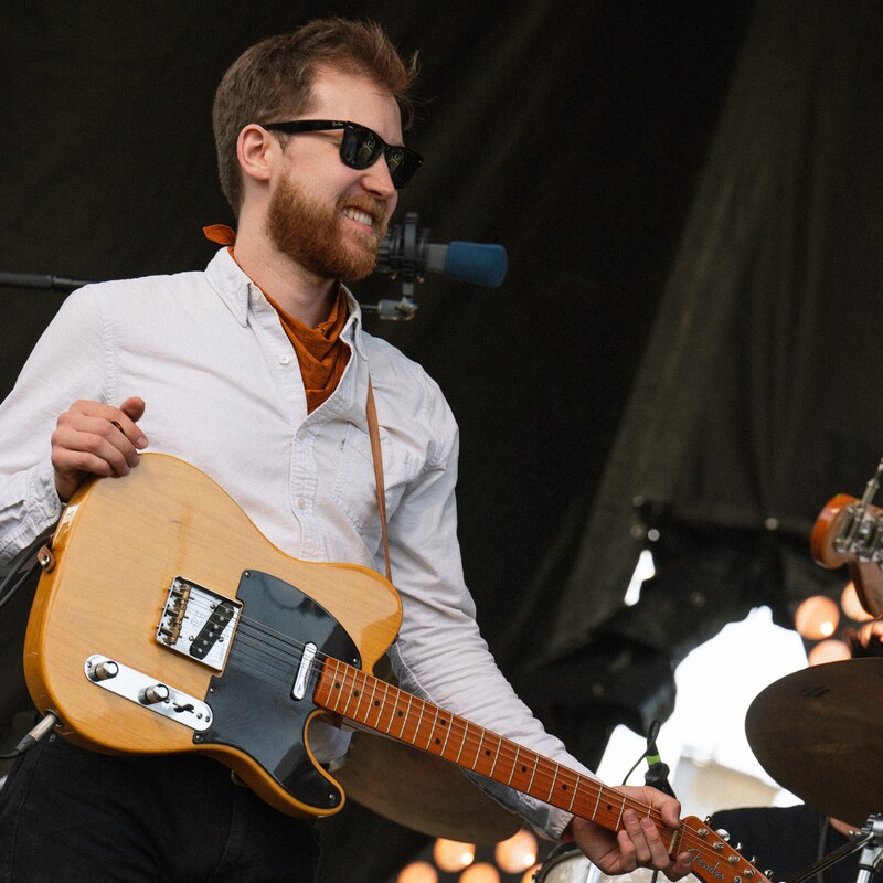 Bryn Besse - Guitarist on stage wearing sunglasses and holding a guitar.