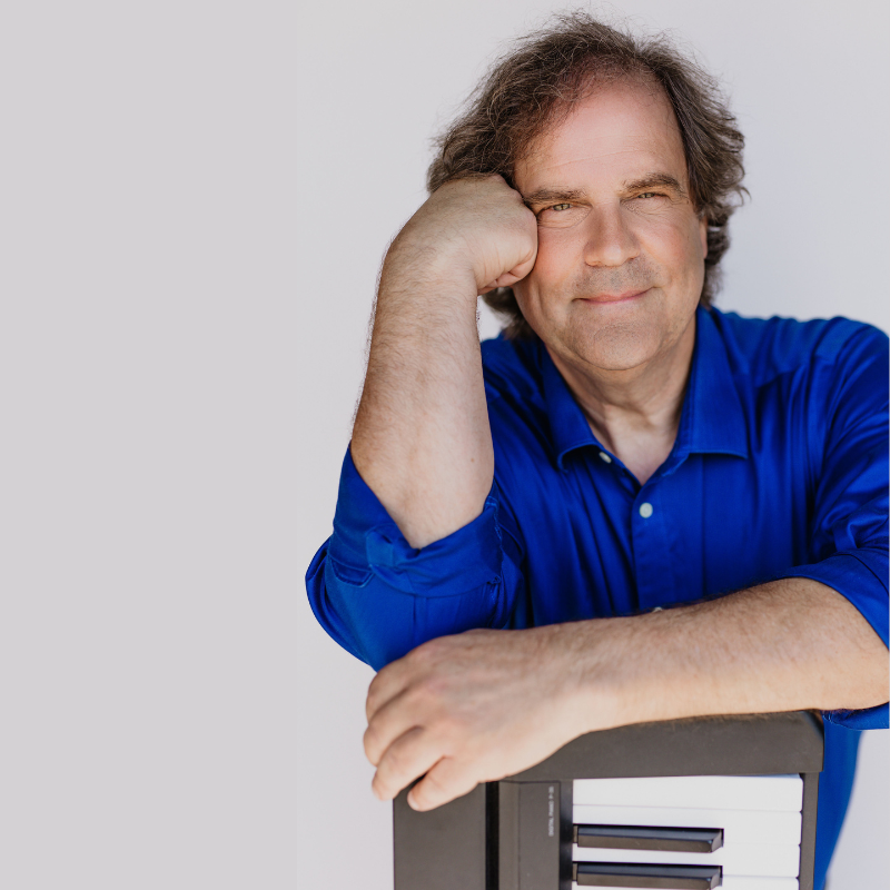 Craig Salkeld by Erin Crooks Photography - Older man in blue chair sitting on chair and resting arms on a piano. 