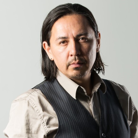 Curtis Peeteetuce  - SK Arts 75th anniversary nominator - Headshot of indigenous man wearing a cream and black three-piece suit with a bow tie and suit without the jacket. Hi medium length hair is combed back.