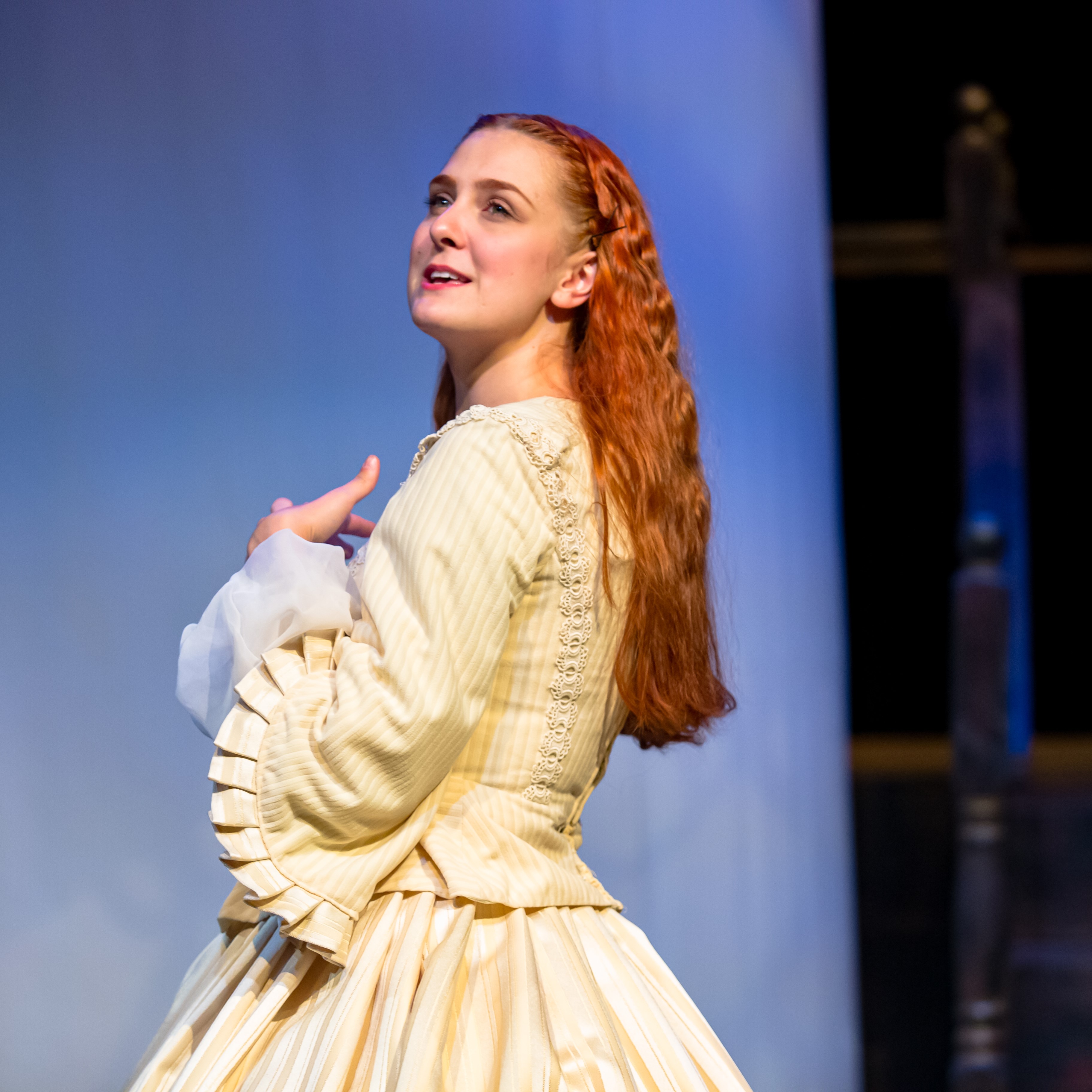 Elizabeth Chamberlin - Young woman with long red hair mid performance on a stage wearing a vintage yellow dress.