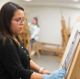 Fine Arts Department - Young woman with brown hair wearing blue gloves drawing on a canvas with charcoal