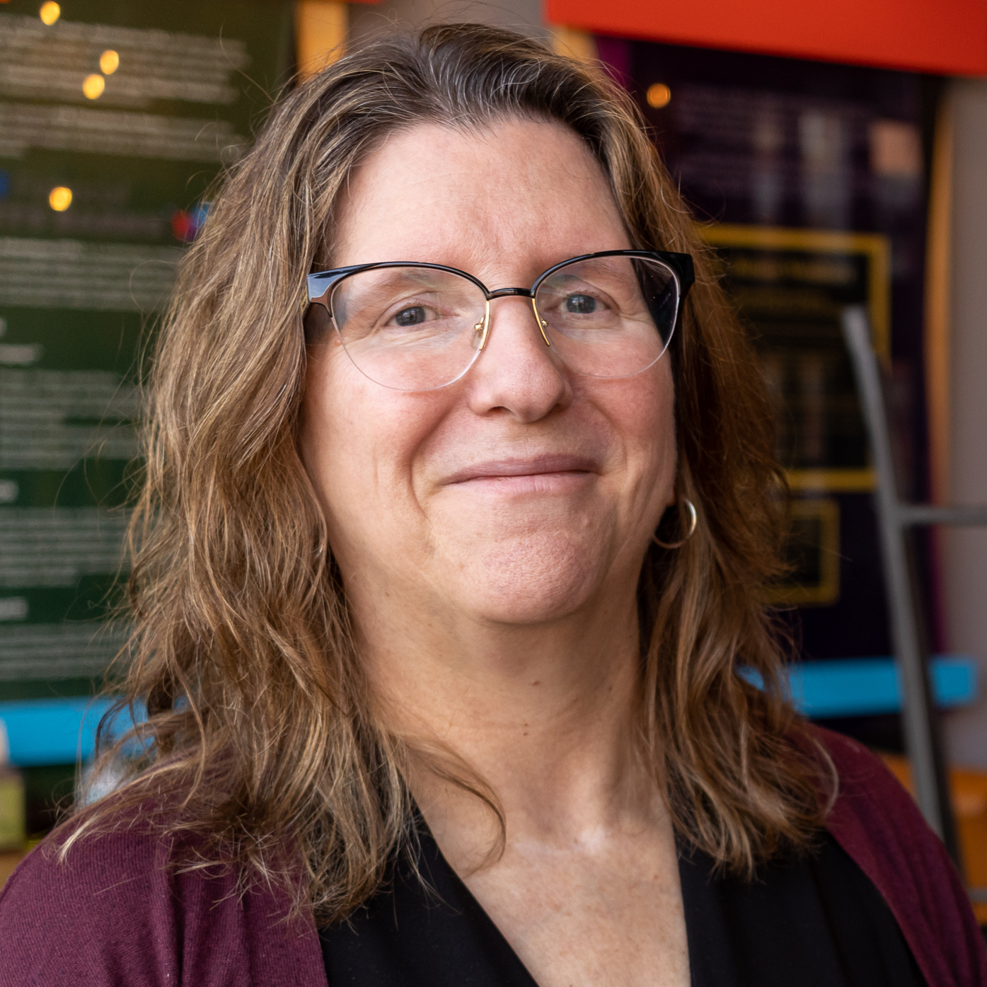 Joanne Weber - Woman with long brown curly hair wearing glasses and smiling.