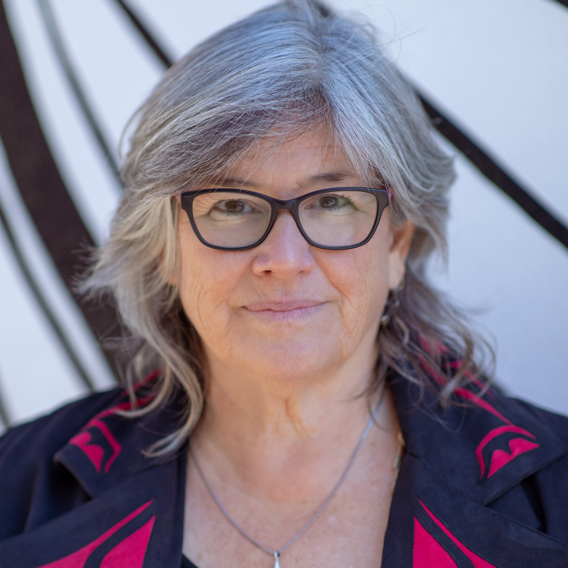 Yvette Nolan - Older white woman with gray hair wearing glasses and smiling.