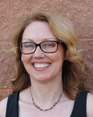 Judy McNaughton - picture of white presenting blonde woman in dark rimmed glasses smiling