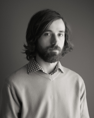 Black and whoite portraite of white presenting male with medium length dark hair, mustache and a beard. - Simon Garez credit to Yves Garez