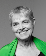 SK Arts board member Judy McCuskee. Black and white headshot of older woman with sort grey hair smiling and green colourpop top