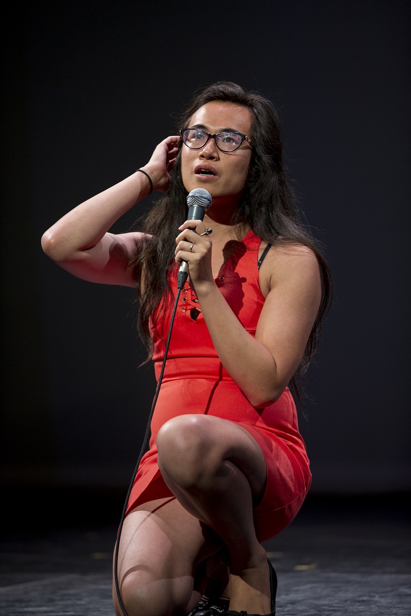 A woman sitting on a stool, performing slam poetry.