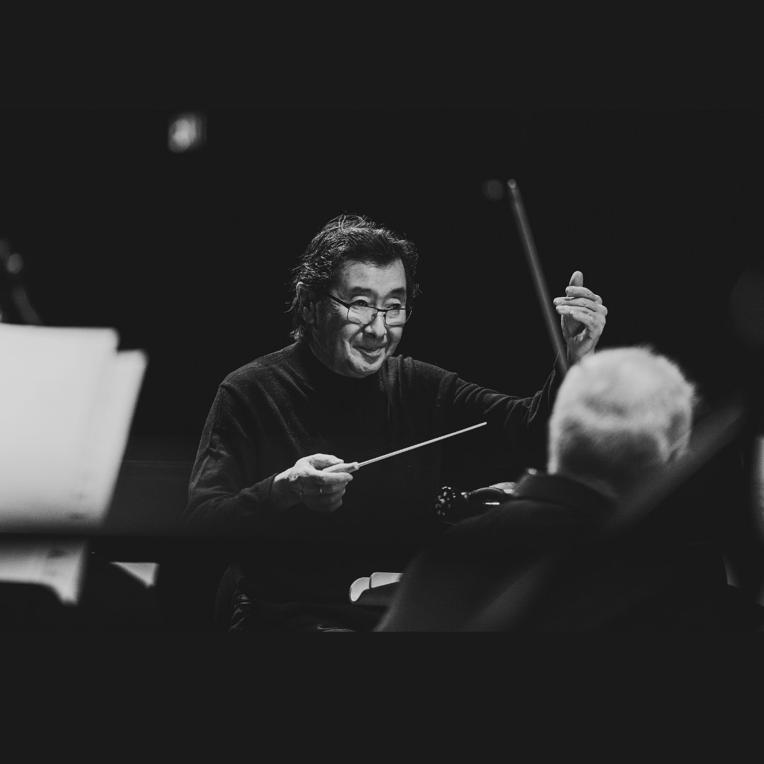 Black and white photo of Victor Sawa, older Asian man with glasses wearing a black ling sleeve shirt and maestro conductor of the Regina Symphony Orchestra mid-conducting performance. Photo courtesy of the RSO posted on SK Arts website, www.sk-arts.ca