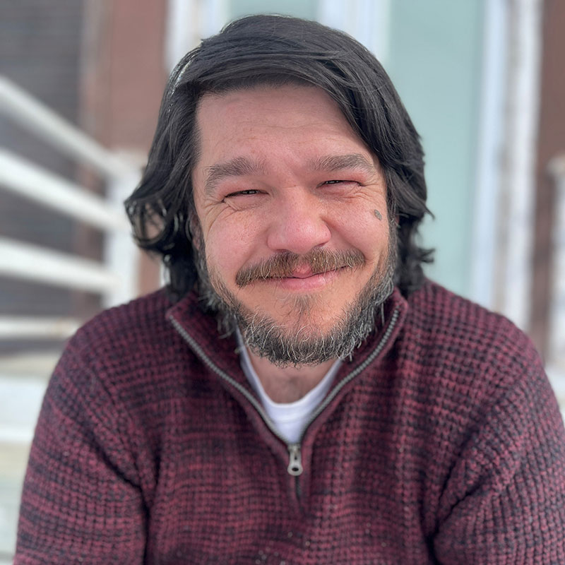 Tim Blackett - Portrait of smiling man with dark hair wearing a burgundy knitted sweater