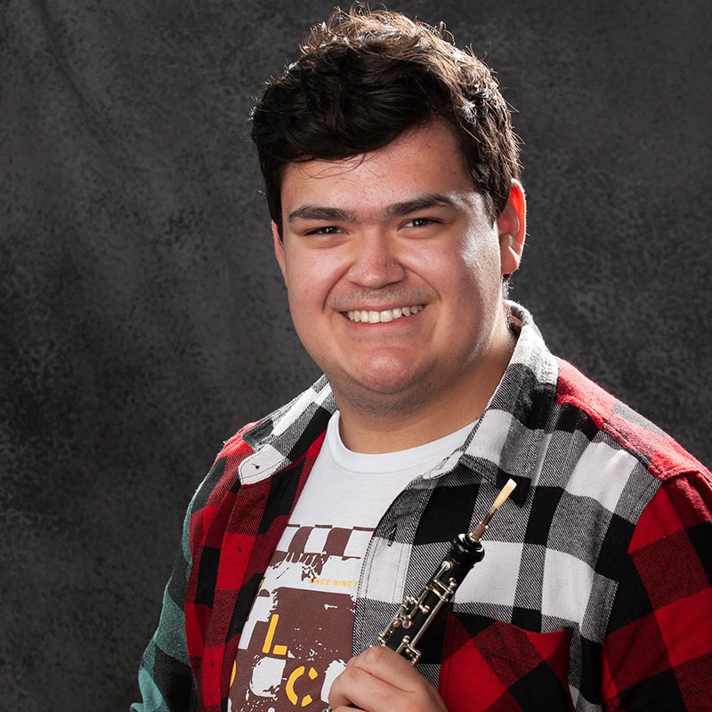 Tyrell Hardlotte - Portrait of young man smiling wearing red, white and black plaid, holding an oboe